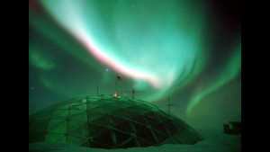 A picture of the aurora over top of a dome structure in the snow
